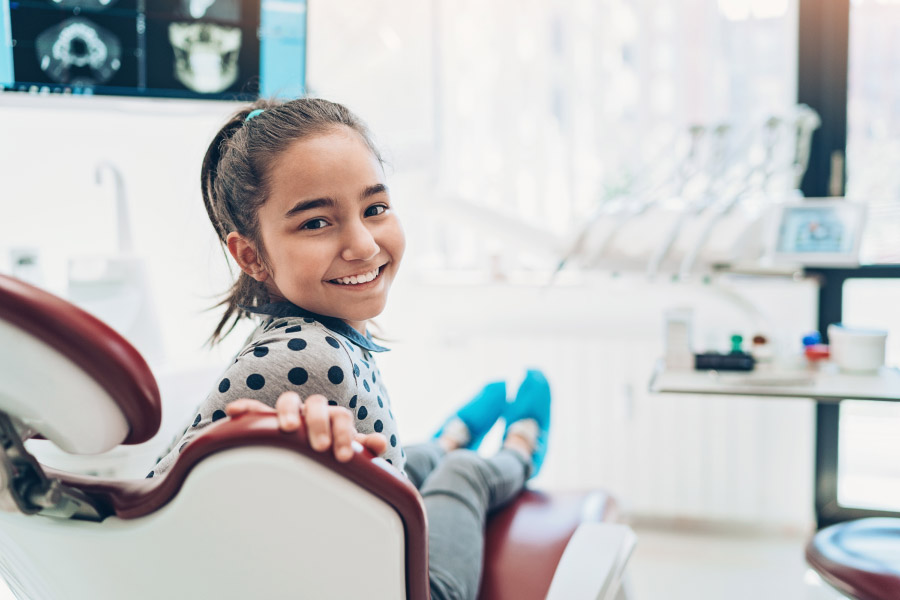 Brunette girl smiles while sitting in the dentist chair at her pediatric dentist in Lytle, TX